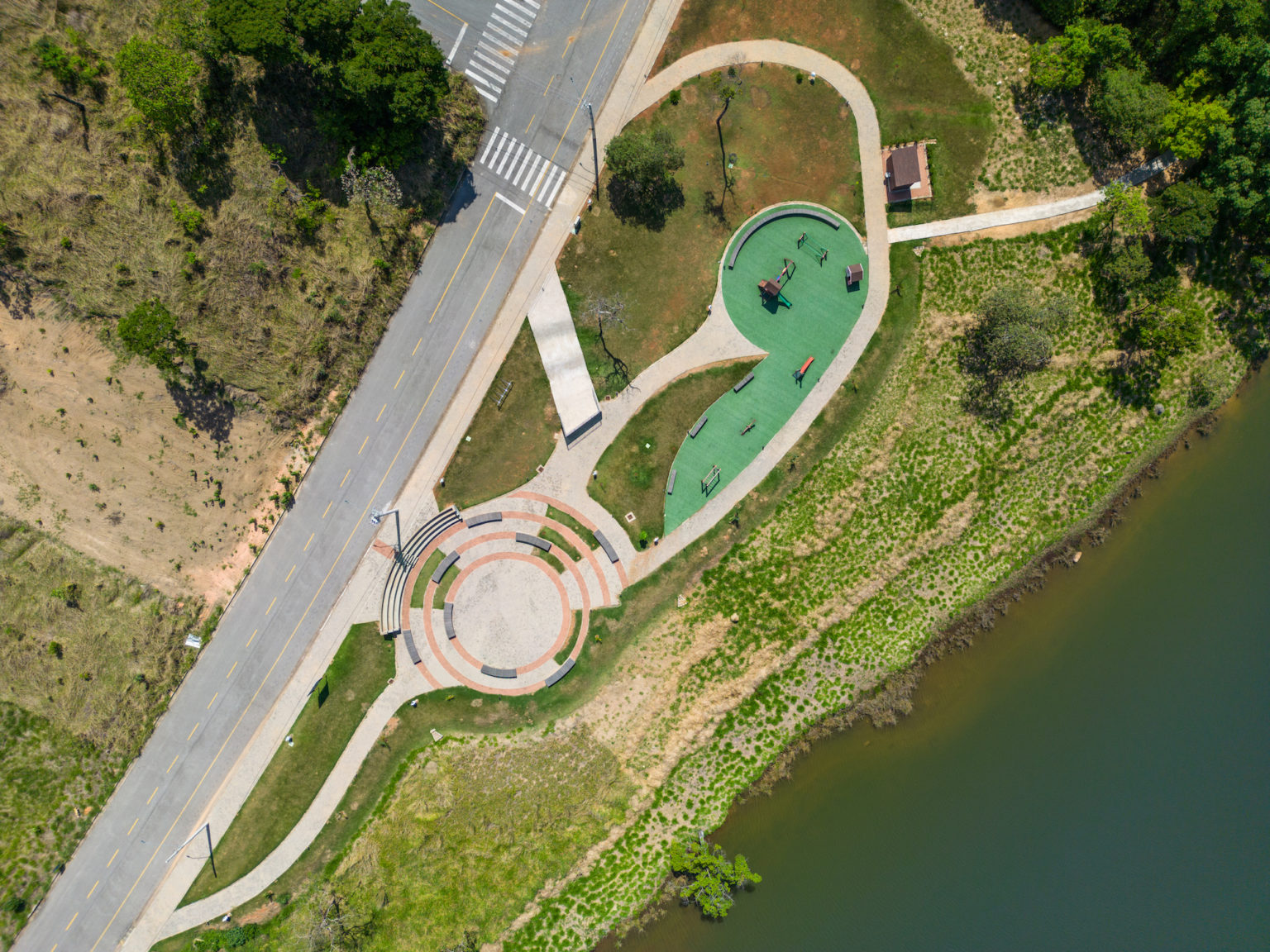 Vista de topo da área de parquinho, com piso verde, pequeno mirante, área de anfiteatro, com arquibancada circular e mais alguns bancos rodeando o centro e pequeno quiosque de apoio